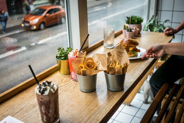 Vindueskarmen ud mod Istedgade med milkshakes, fritter og en gæst der rækker ud efter sin burger